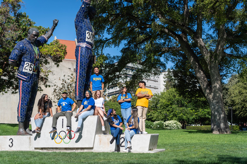 A diverse group of students sit around our Statue of John Carlos and Tommie Smith. 