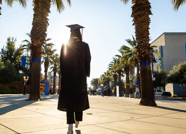 An SJSU graduate walking towards the sun on campus.