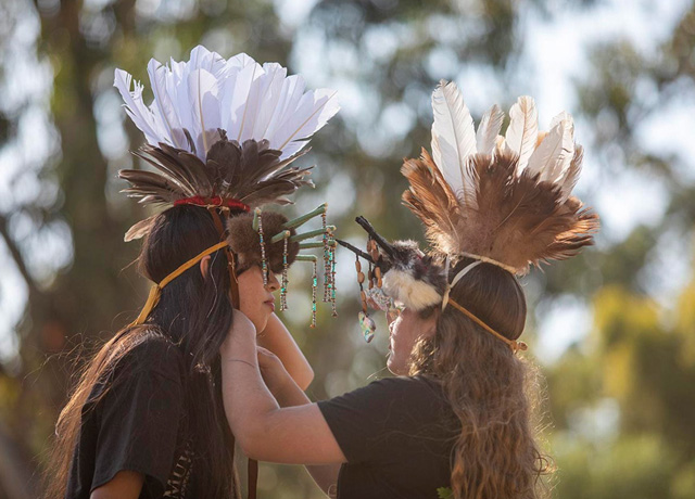Gianna Ramirez, a Miwok Tribe member from Sacramento, helps Muwekma Ohlone Tribe member Isabella ‘Amne Gomez adjust her headdress.