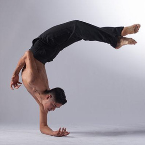 Choreographer and dancer holding himself up by one arm as his body bends upside down in a curve form.