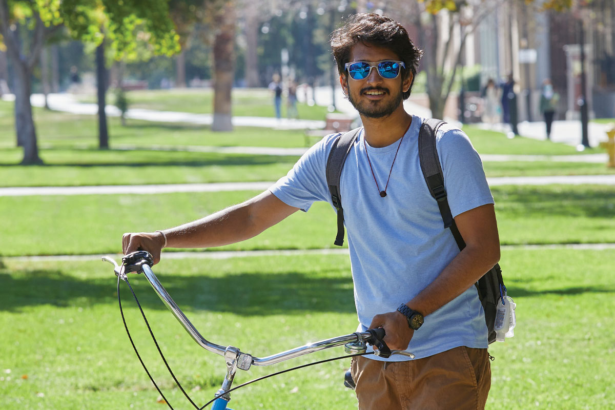 Student wearing shades holding up a cruiser bike.