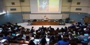 Faculty member giving a lecture in front of a large class in a lecture hall.  