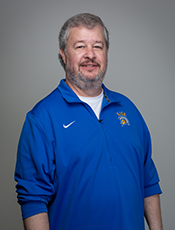 waist-up photo of John Gibbs, Caucasian Male with short gray hair and short beard, wearing blue Spartan track jacket with a white undershirt