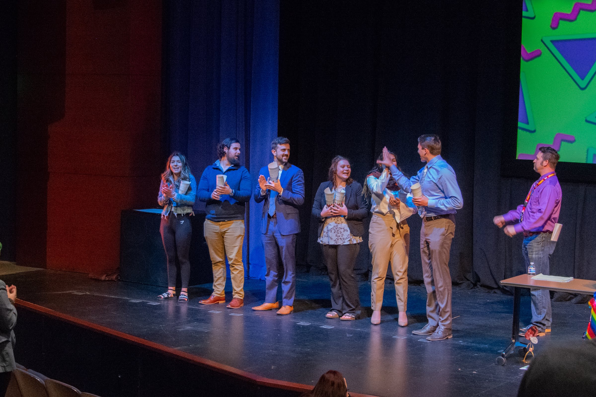 Forensics members standing on stage with a host high-fiving a participant.