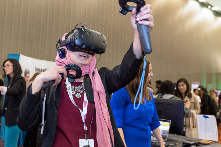 Female student wearing VR goggle holding a control in each hand.