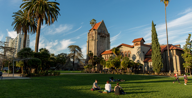 Three people sitting in the grass in front of Tower Hall on the SJSU campus.
