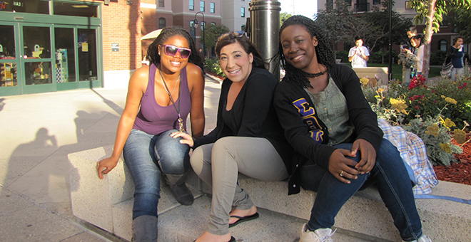 Three students sitting on a bench outside of a building on campus.