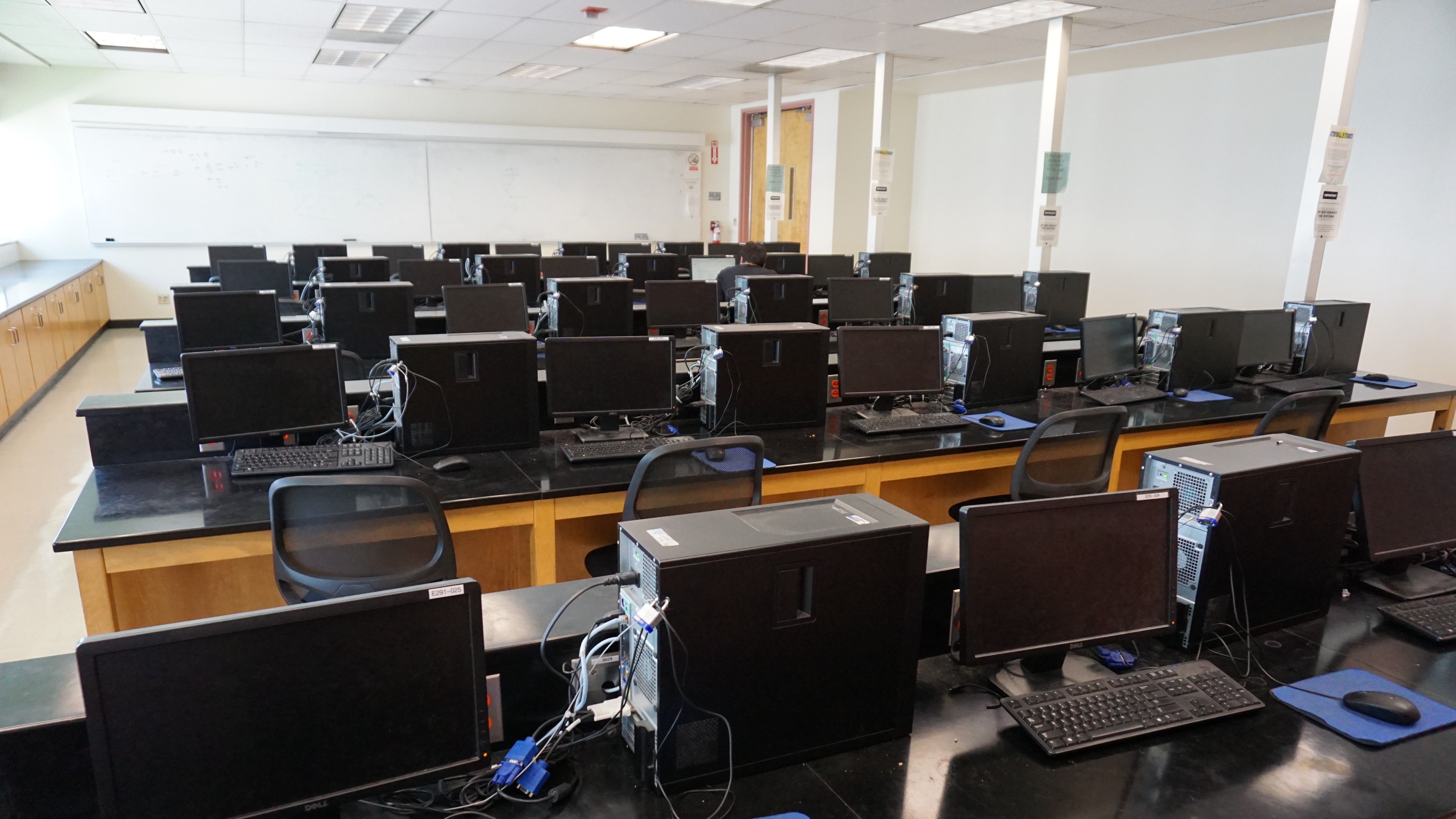 A classroom full of computer stations with whiteboards hanging on every wall.