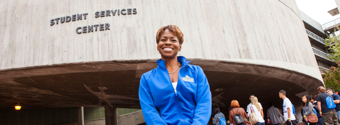 A smiling staff member standing in front of the student services center.