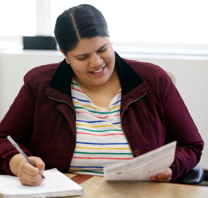A woman smiles while taking notes.
