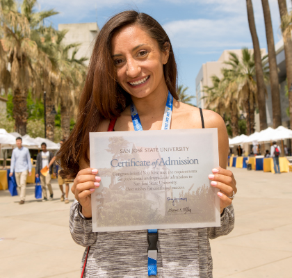 student smiling, holding a certificate of admission to SJSU. 