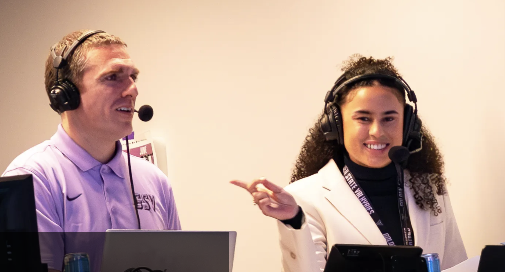 one smiling woman pointing at a man talking into a head mic