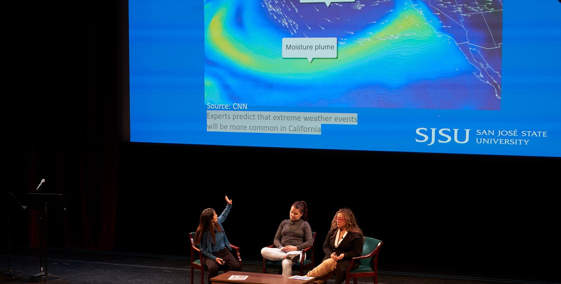 3 people on a stage seated with image of water behind them