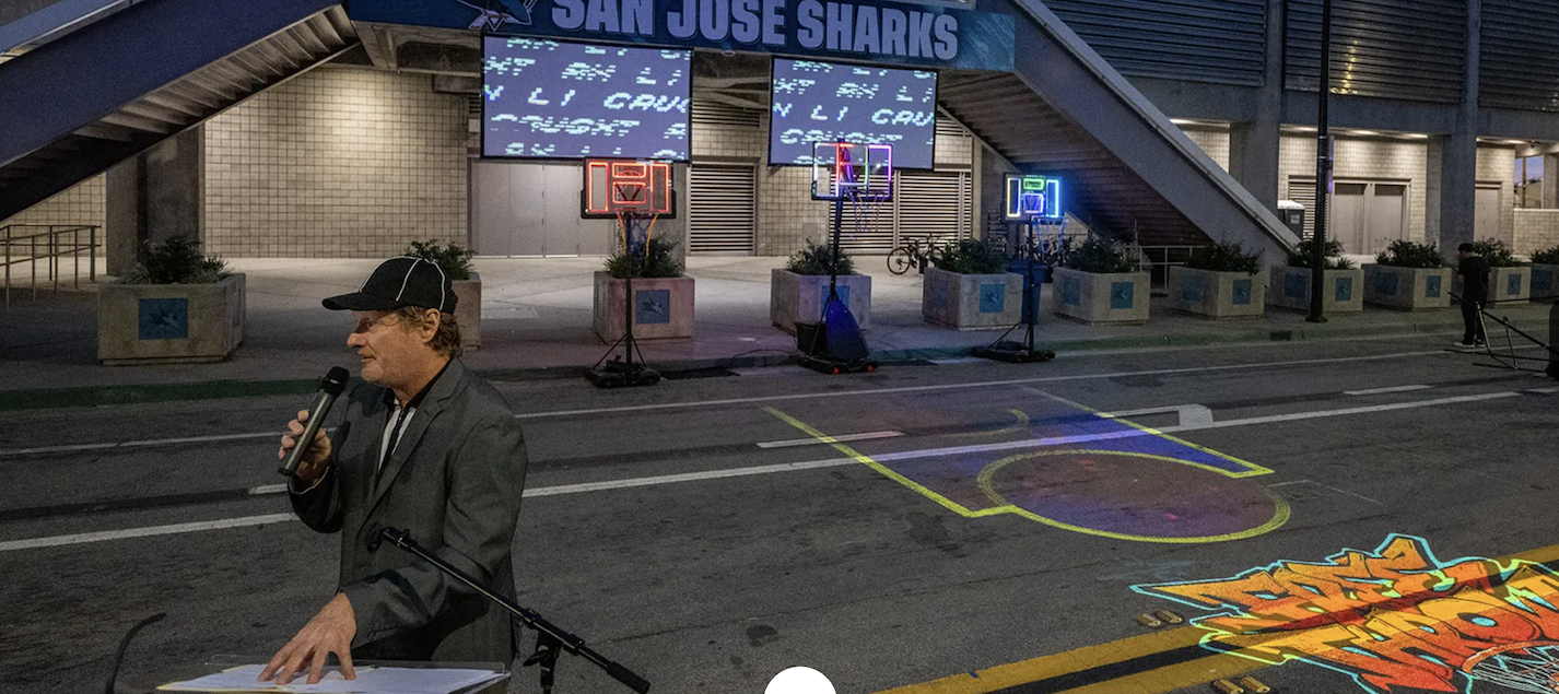 craig hobbs in front of podium with artwork to the left and san jose sharks above on a dark street