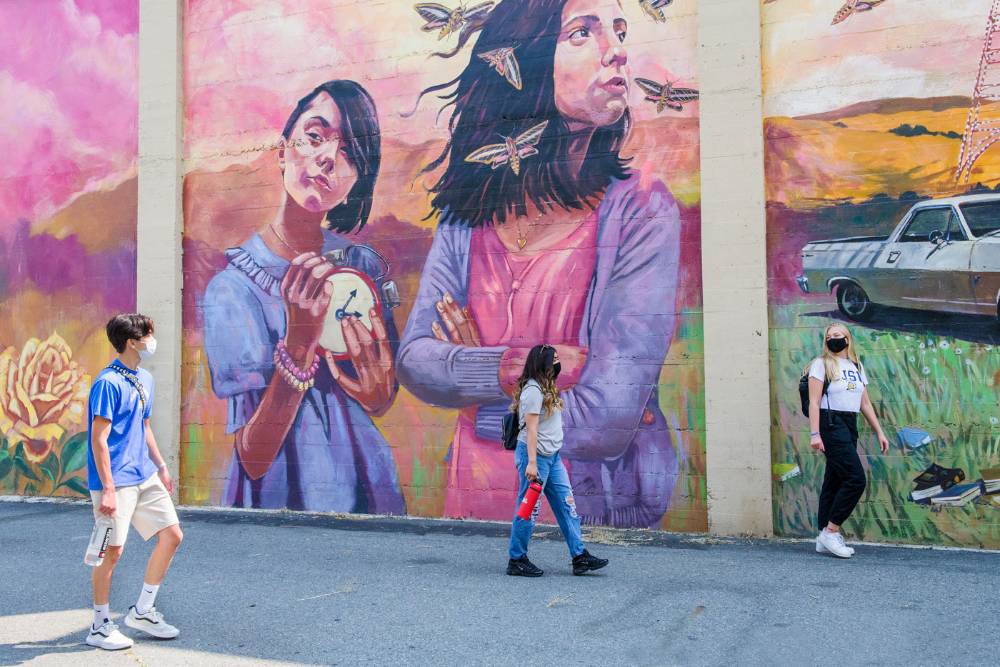 Students roaming downtown in front of a colorful mural.