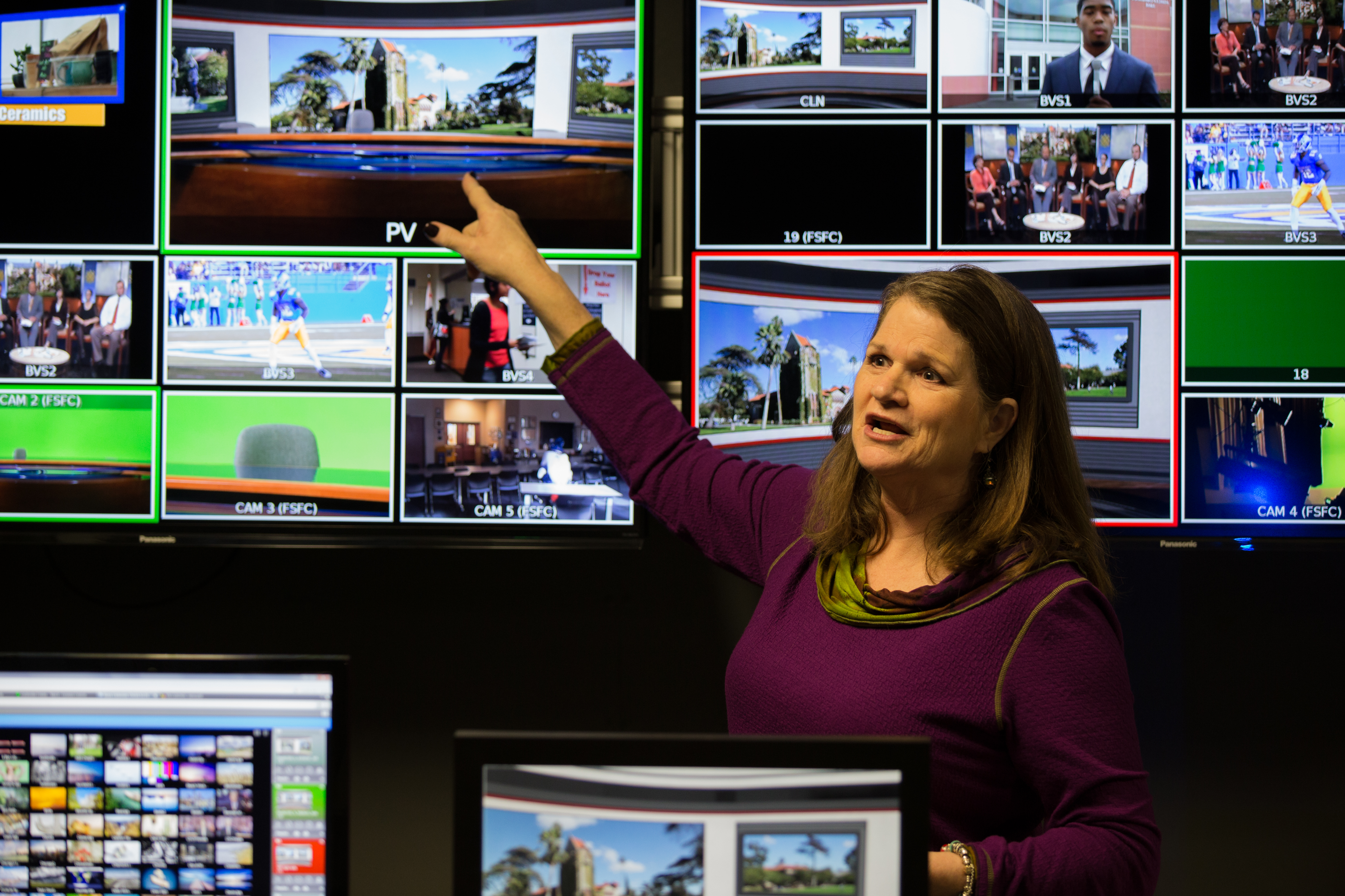 A female professor points towards one of many monitors in a television studio. 