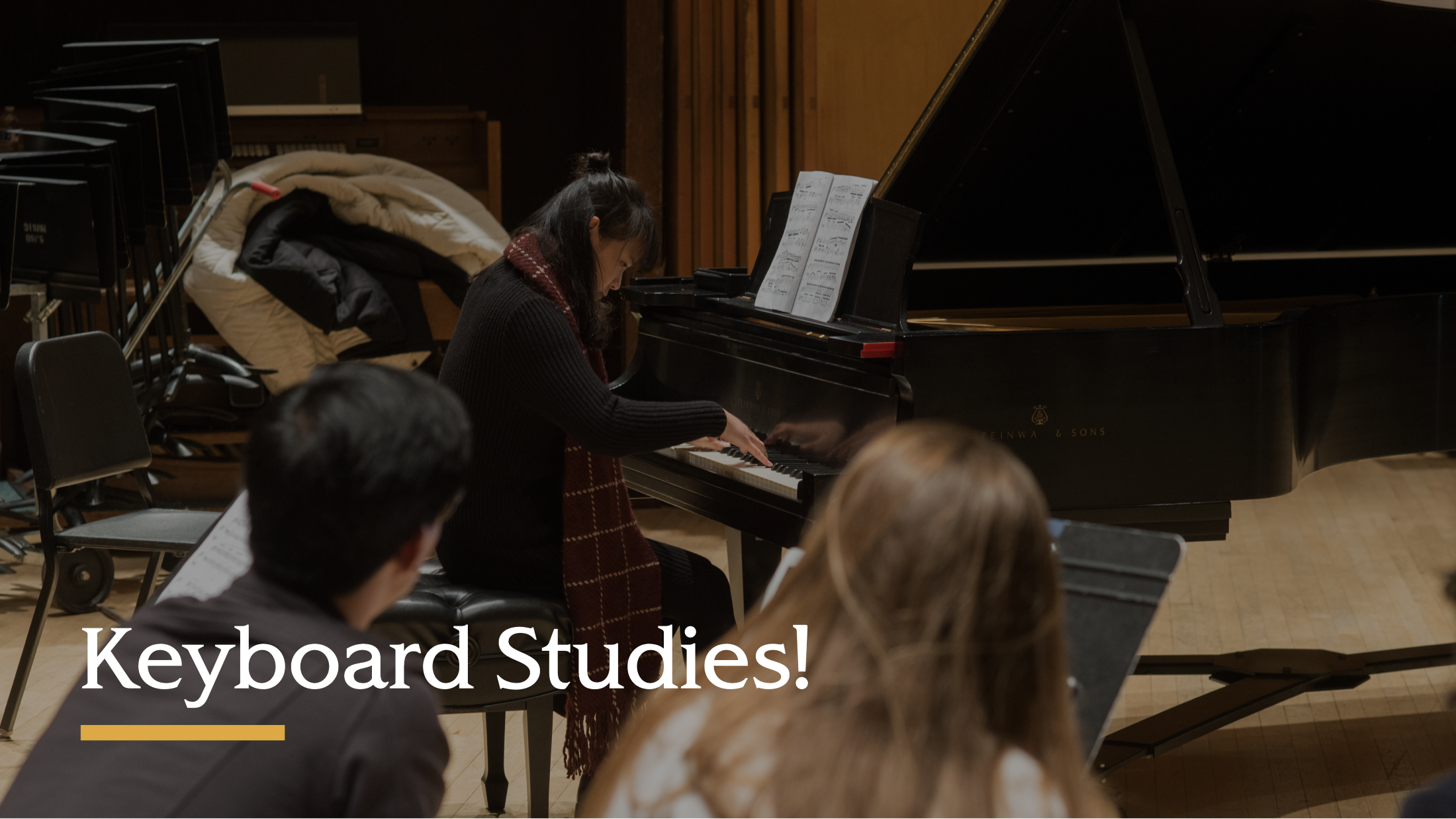 Student playing a grand piano while other students watch.