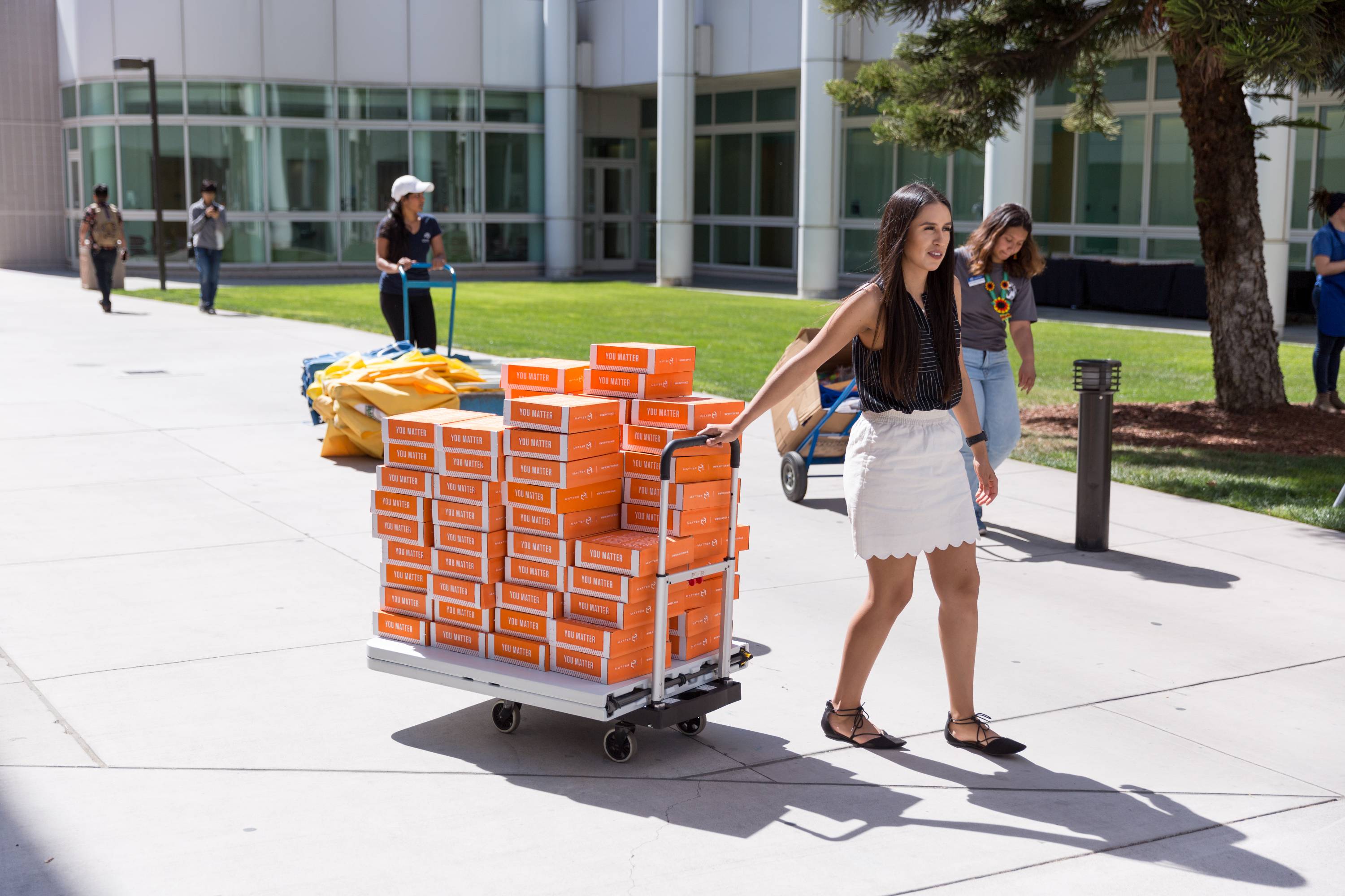 Female students pull dollies outside filled with boxes of food.