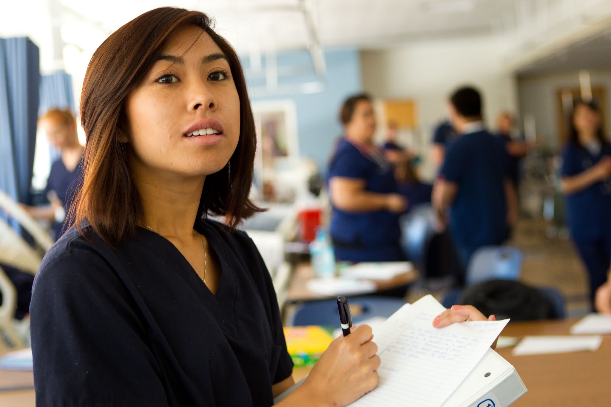 Image of nursing student in scrubs takes notes in a binder.