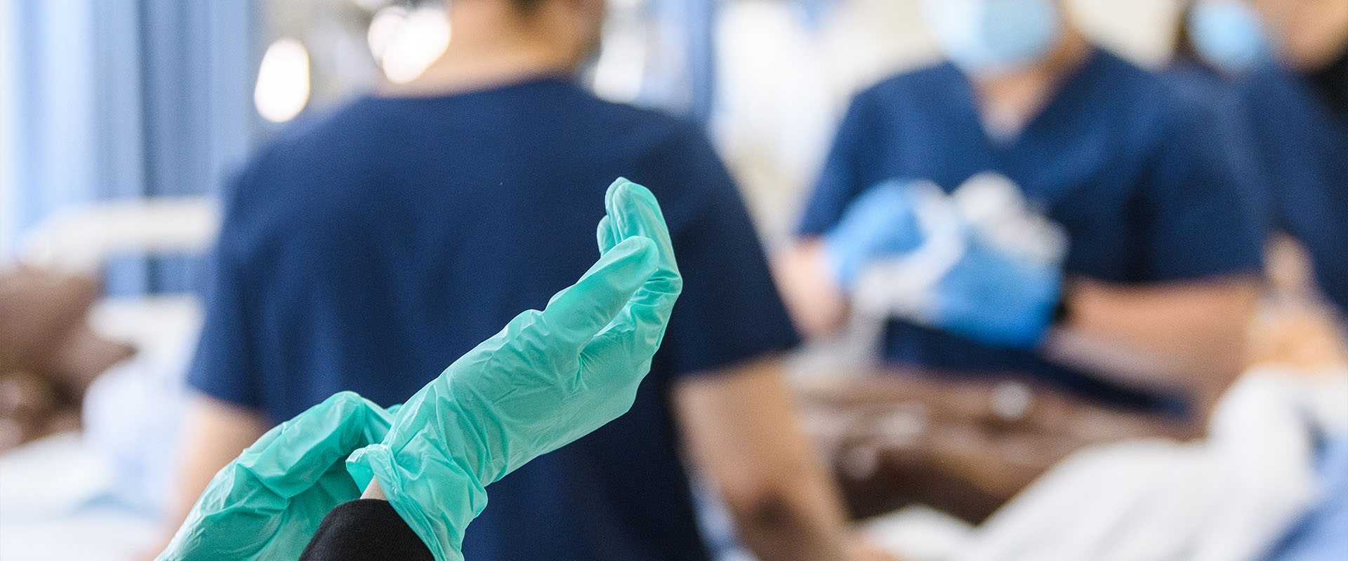 Gloved hand with SJSU nursing students in the background