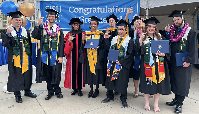 Students and faculty members pose in graduation regalia.