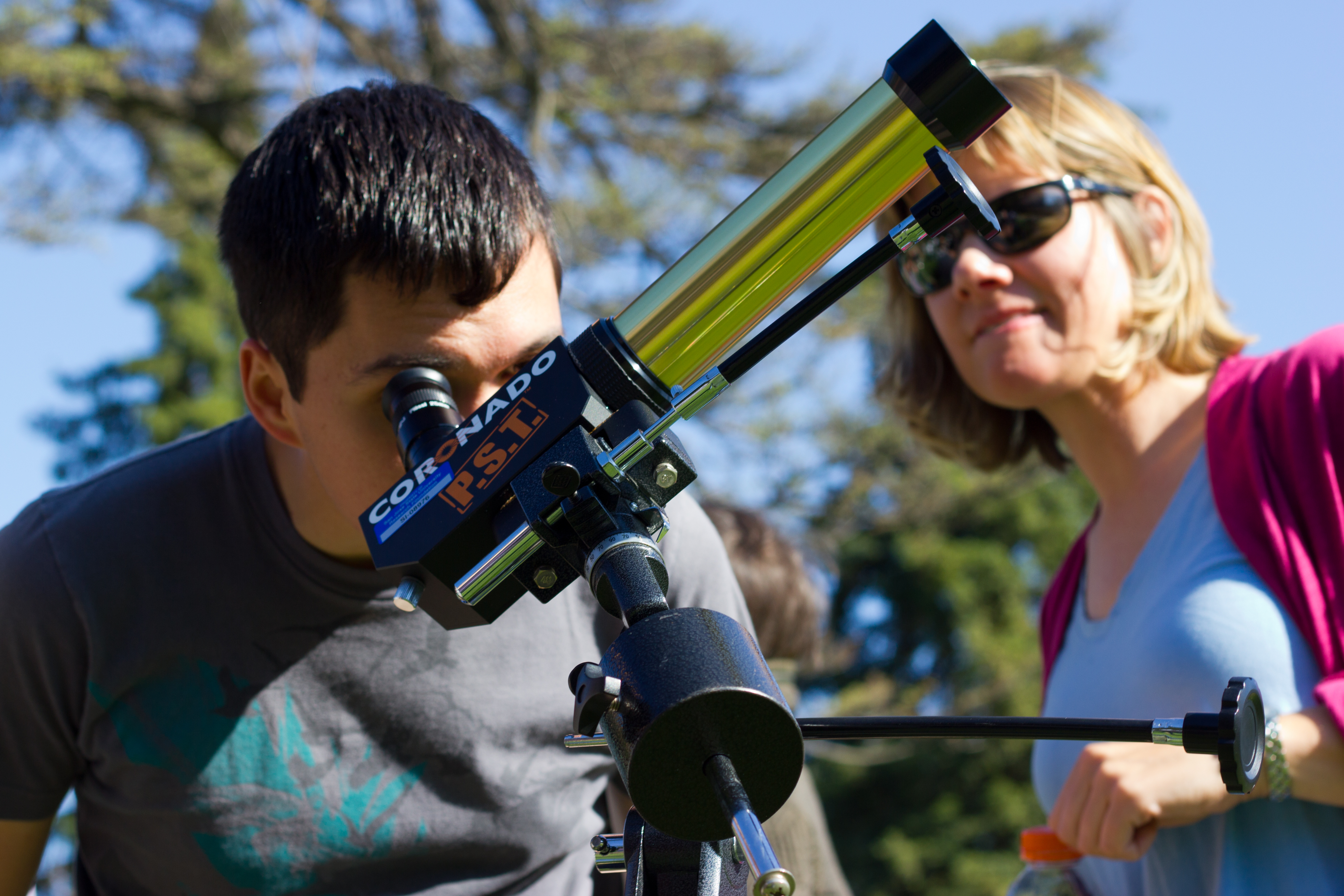 A male student is looking through a telescope while a female professor observes. 