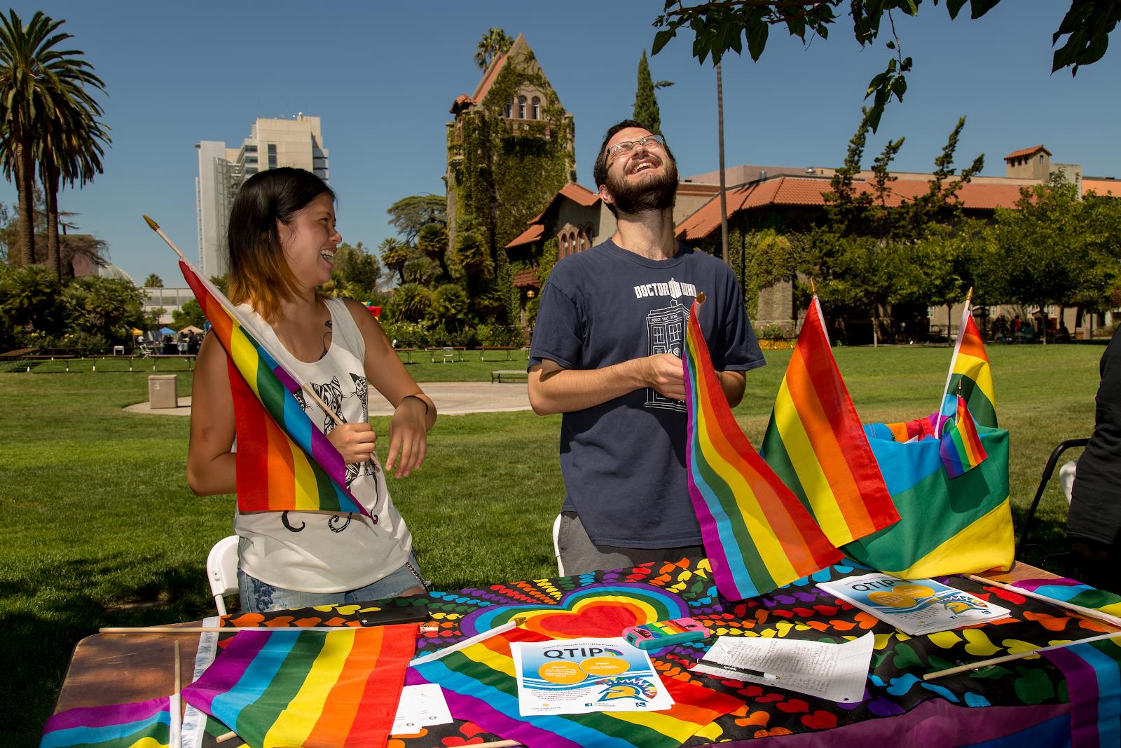 Students tabling for student org laughing and holding rainbow flags.