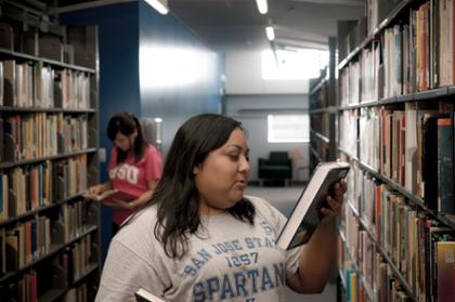Photo of student in library holding and looking at book.