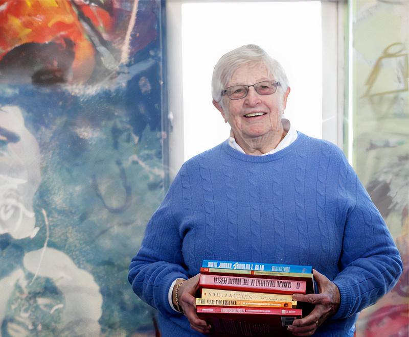 Portrait of Wiggsy Sivertsen with lightblue sweater holding a stack of books.