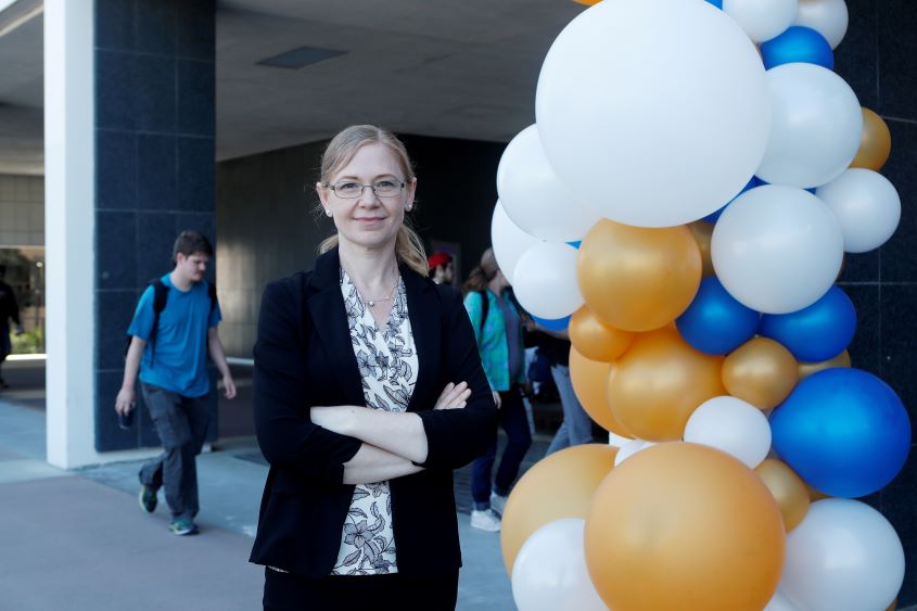 Dr. Miri VanHoven standing next to white, blue and gold mylar balloons.