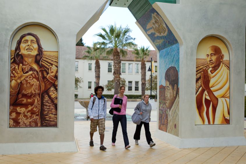 Three students walk through the Chavez Arch on campus.