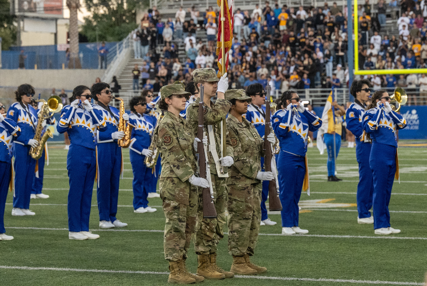 SJSU armed servicemembers stand with the American flag. 