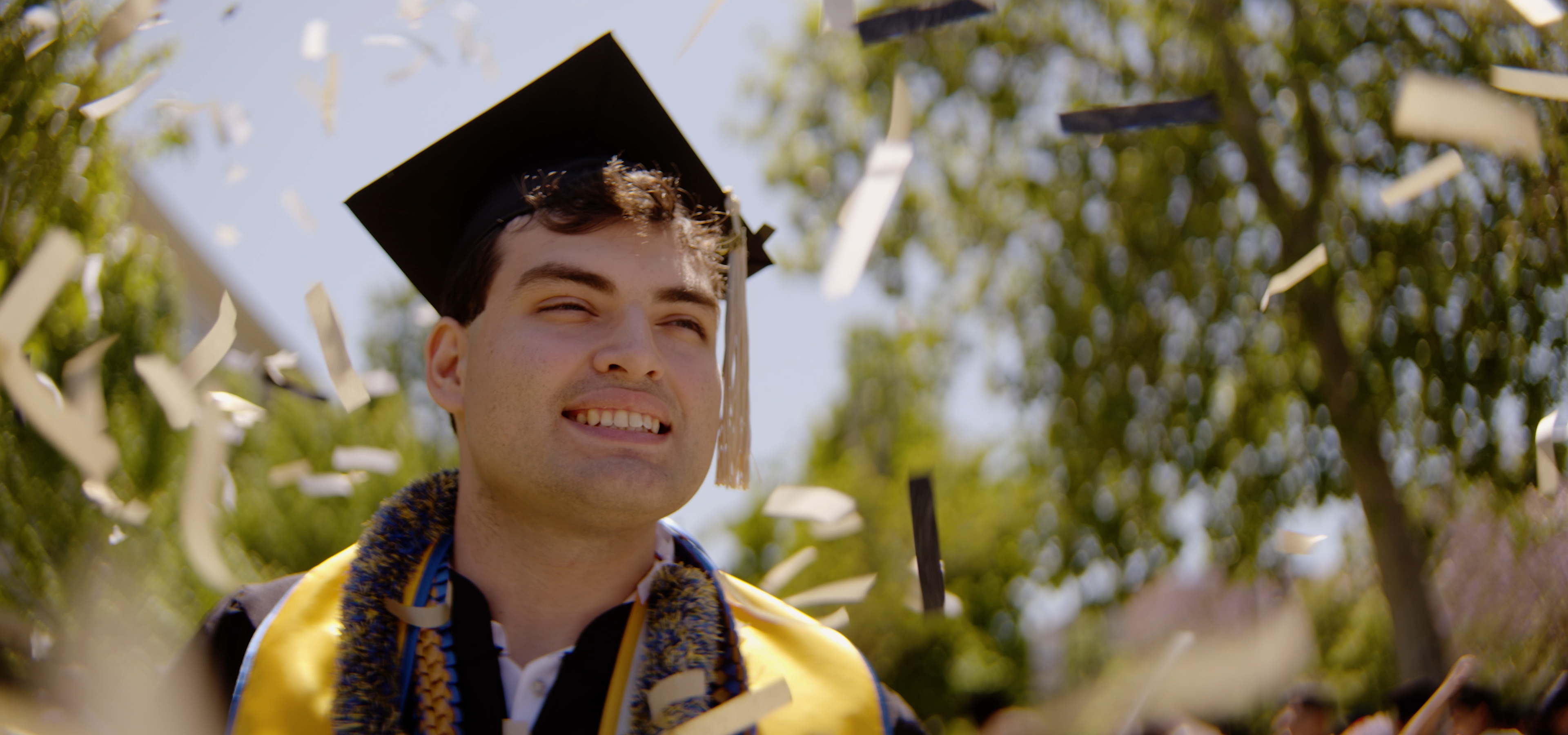 San Jose State University male graduate smiling with gold confetti in the air. 