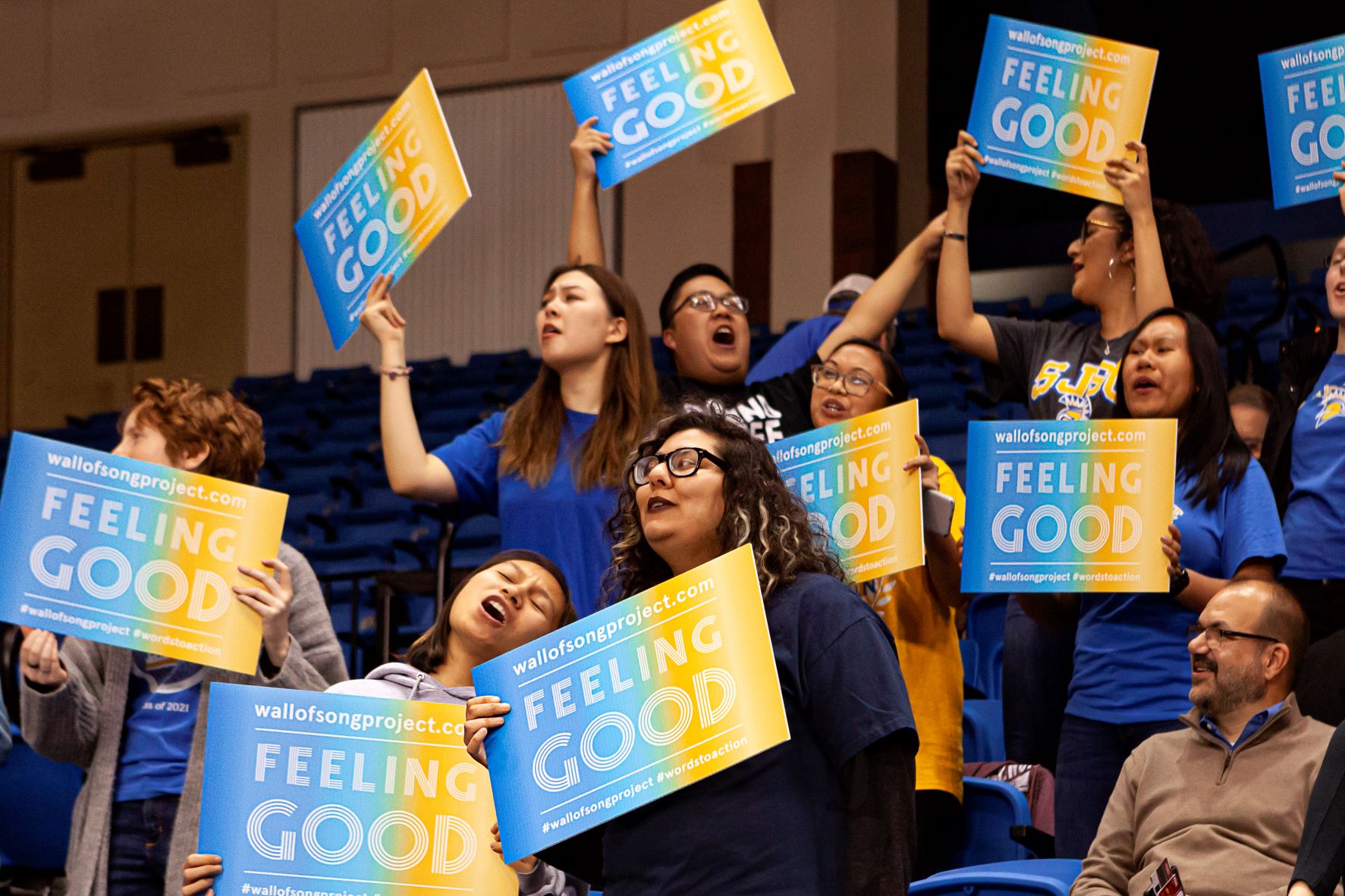 Crowd of people singing while holding 'Feeling Good' signs