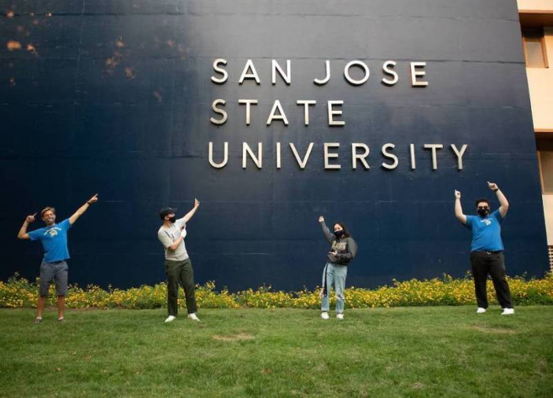 SJSU students wear masks on campus pointing to a San Jose State University sign