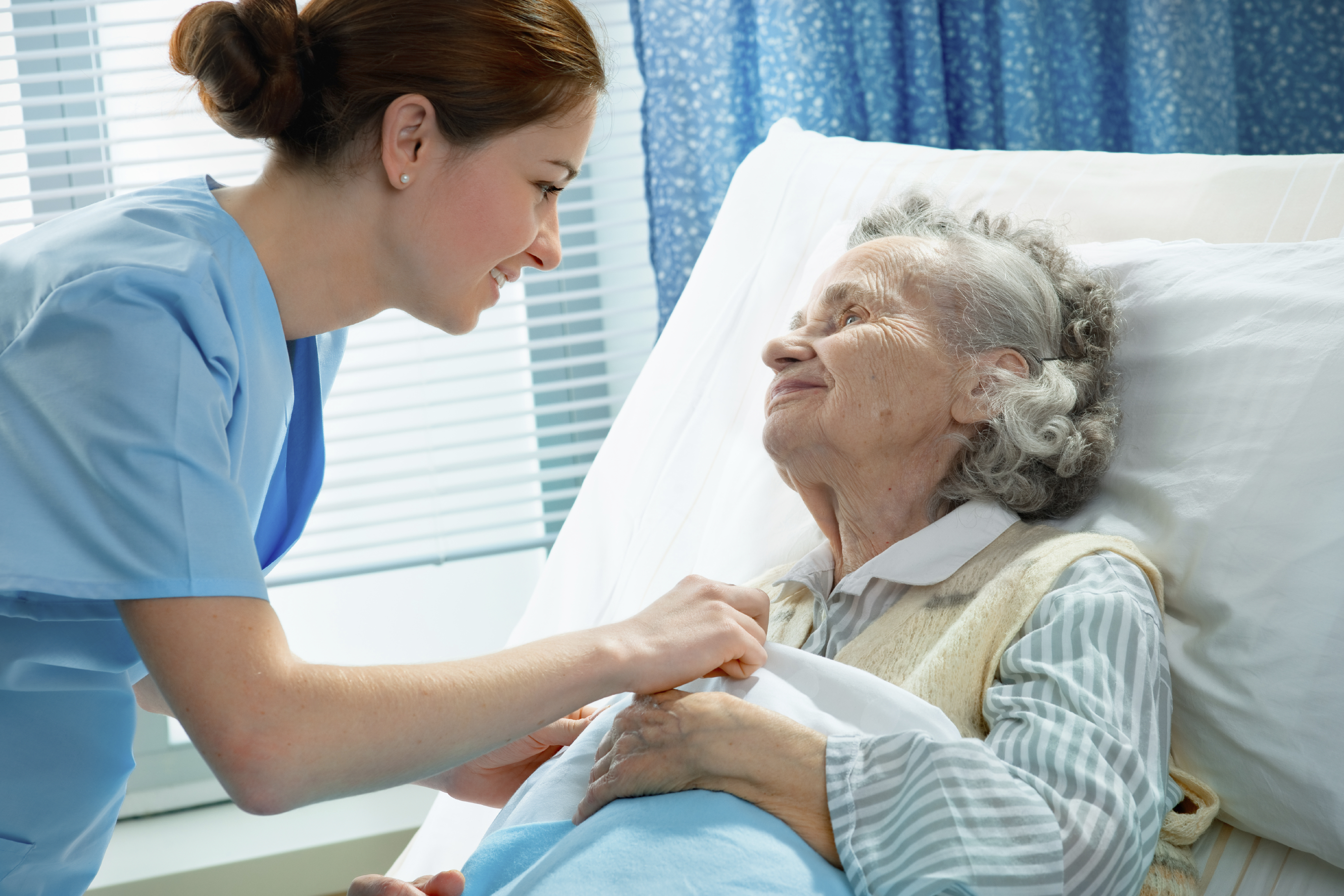 Nurse smiling at an elderly patient in a hospital bed.